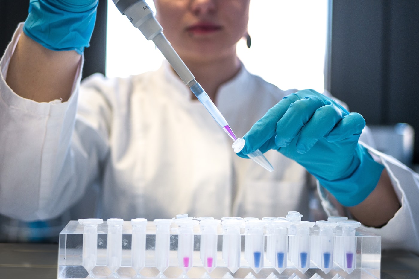 A scientist using a pipette beside test tubes in a laboratory.